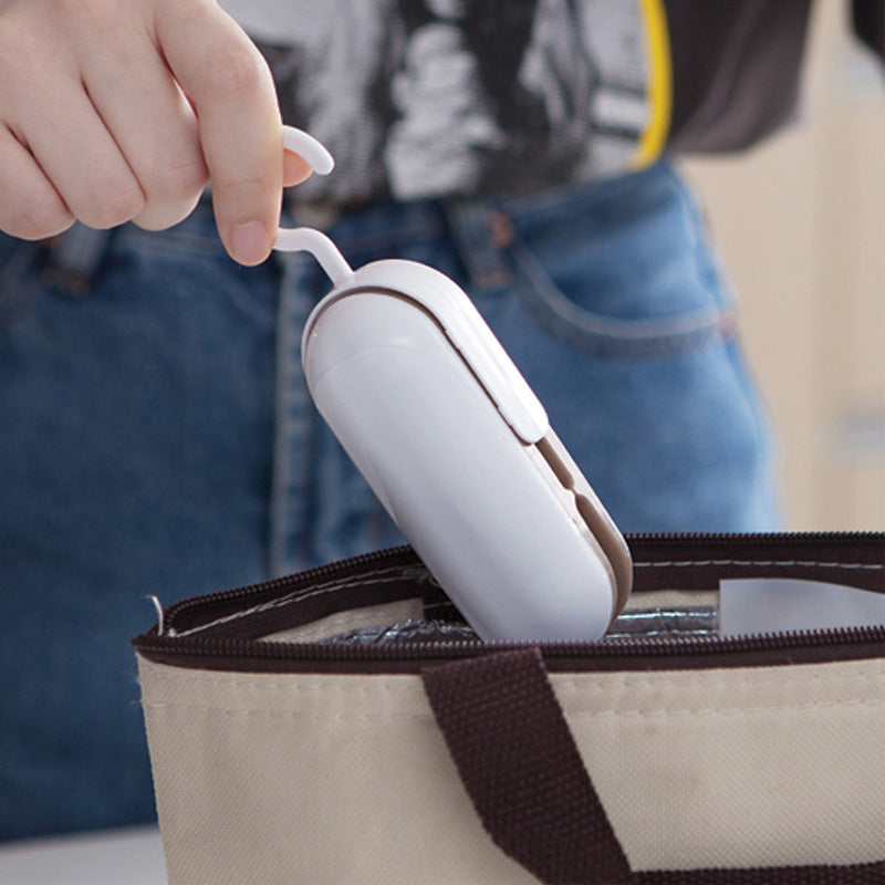 Mini portable heat sealer in white held above a bag opening for sealing