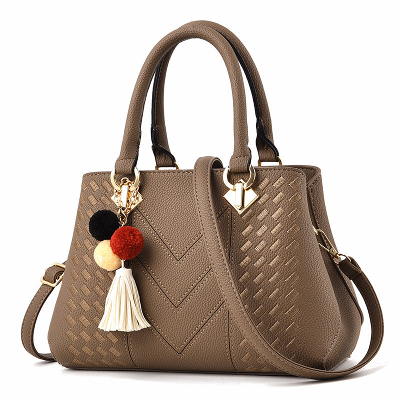 Khaki quilt-textured handbag with top handles, crossbody strap, and pom tassel charm