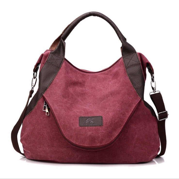 Burgundy canvas shoulder bag with dark trim, top handles, and side zipper pockets