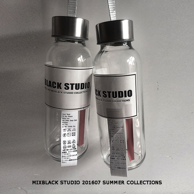 Two clear glass water bottles with black lids and front labels