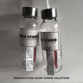 Front view of two clear glass water bottles with black screw caps