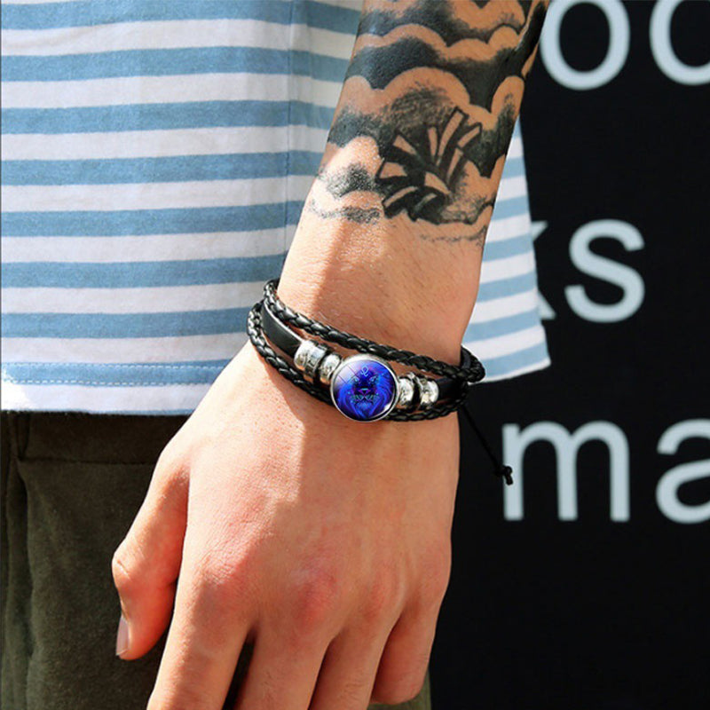 Black braided zodiac bracelet on arm with glowing blue round charm and silver cuffs