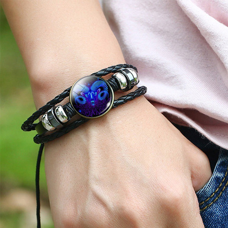 Zodiac charm bracelet on wrist, black braided strap with glowing blue oval medallion