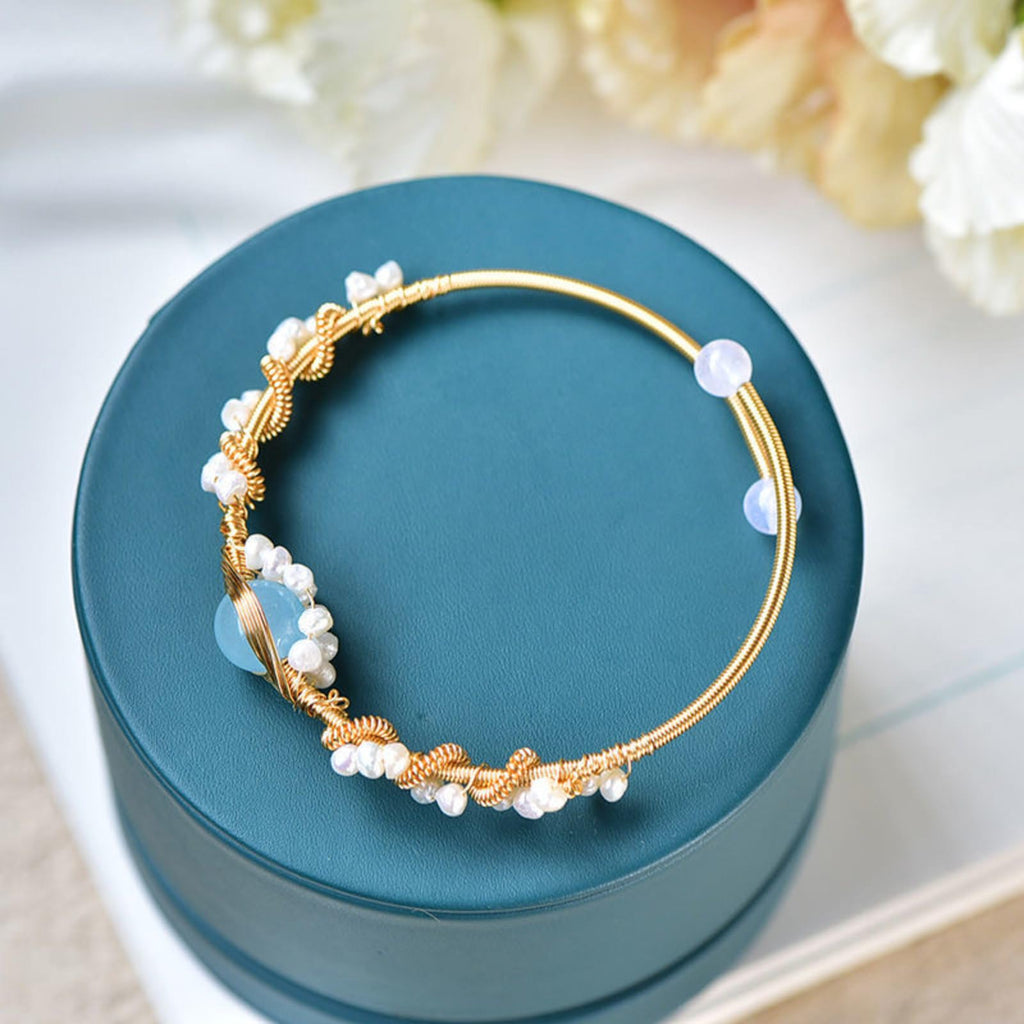Gold pearl cuff bracelet with blue oval charms and white pearls on teal cushion